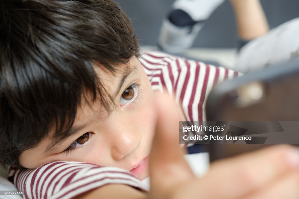 Young boy laying down looking at a smartphone