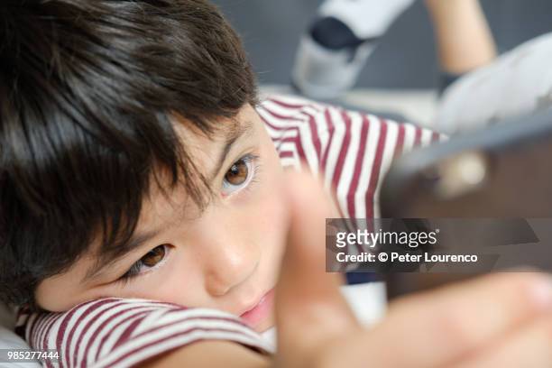 young boy laying down looking at a smartphone - peter lourenco stock-fotos und bilder