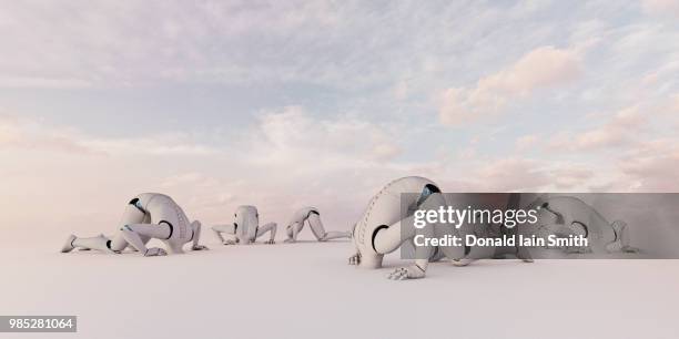 head in the sand: white robots kneeling with head buried in the ground - den kopf in den sand stecken stock-fotos und bilder