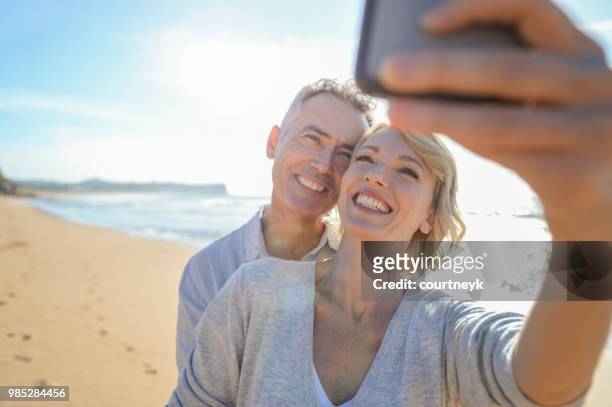 älteres paar unter einem selfie am strand mit einem mobiltelefon - the face of australia photo call stock-fotos und bilder