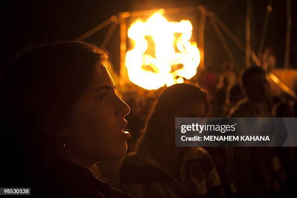 Israeli familes and youths from the Masada scout movement stand in front of a burning inscription symbolising the Israeli army during a ceremony to...