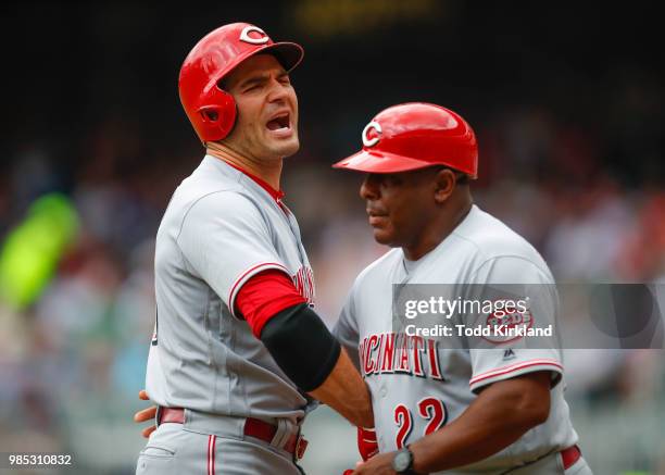 Joey Votto of the Cincinnati Reds is restrained by third base coach Billy Hatcher as he is ejected from the game in the first inning of an MLB game...