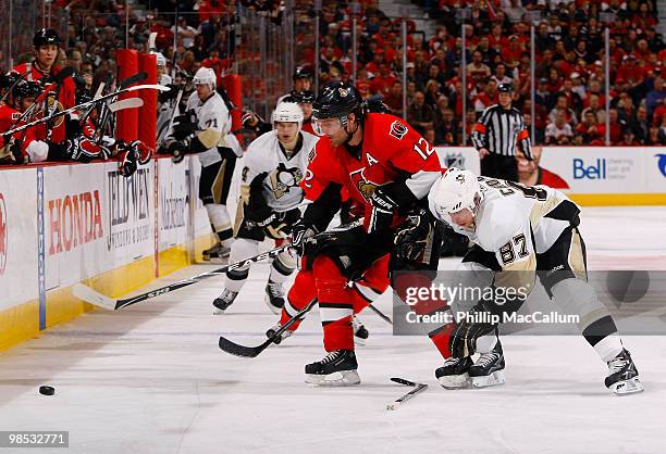 Mike Fisher of the Ottawa Senators tries to control the puck along the boards while battling with Sidney Crosby of the Pittsburgh Penguins during...