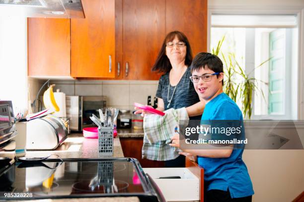 mother helping her son of 12 years old with autism and down syndrome in daily lives emptying the dishwasher - genetic research stock pictures, royalty-free photos & images