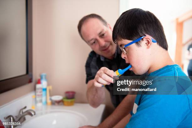 father helping her son of 12 years old with autism and down syndrome in daily lives brushing her teeth - brush teeth stock pictures, royalty-free photos & images