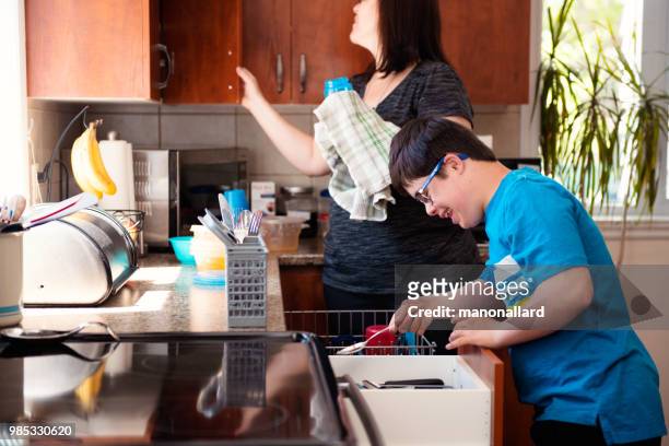 Mother helping her son of 12 years old with Autism and Down Syndrome in daily lives emptying the dishwasher