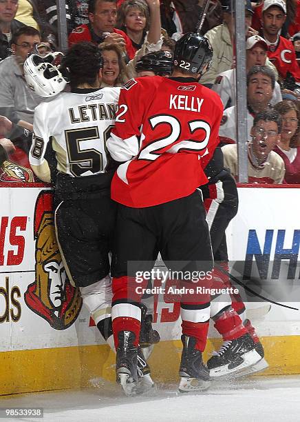 Chris Kelly and Chris Neil of the Ottawa Senators bodycheck Kris Letang of the Pittsburgh Penguins into the boards, knocking his helmet off in the...