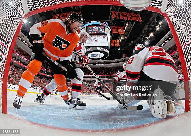 Martin Brodeur of the New Jersey Devils hangs on to the puck as teammate Colin White and Scott Hartnell of the Philadelphia Flyers wait for a rebound...