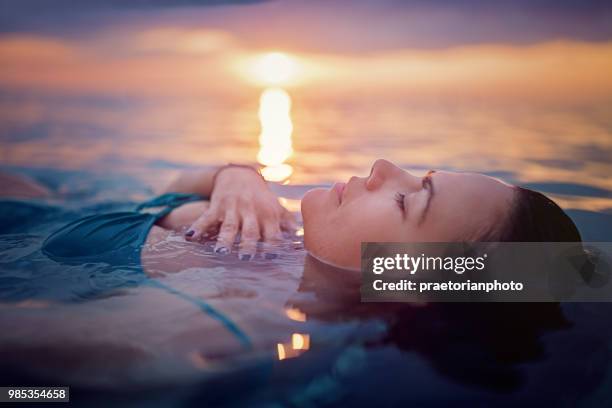 woman is lying and relaxing in the ocean at the front of a beautiful sunset - bottomless girl stock pictures, royalty-free photos & images