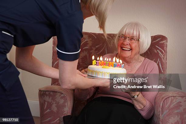 elderly woman receiving birthday cake from a carer - bob bradford - fotografias e filmes do acervo