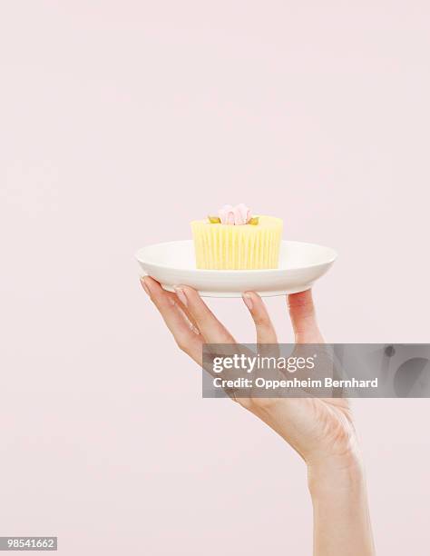 female hand holding cupcake on a white plate - donna piatto foto e immagini stock