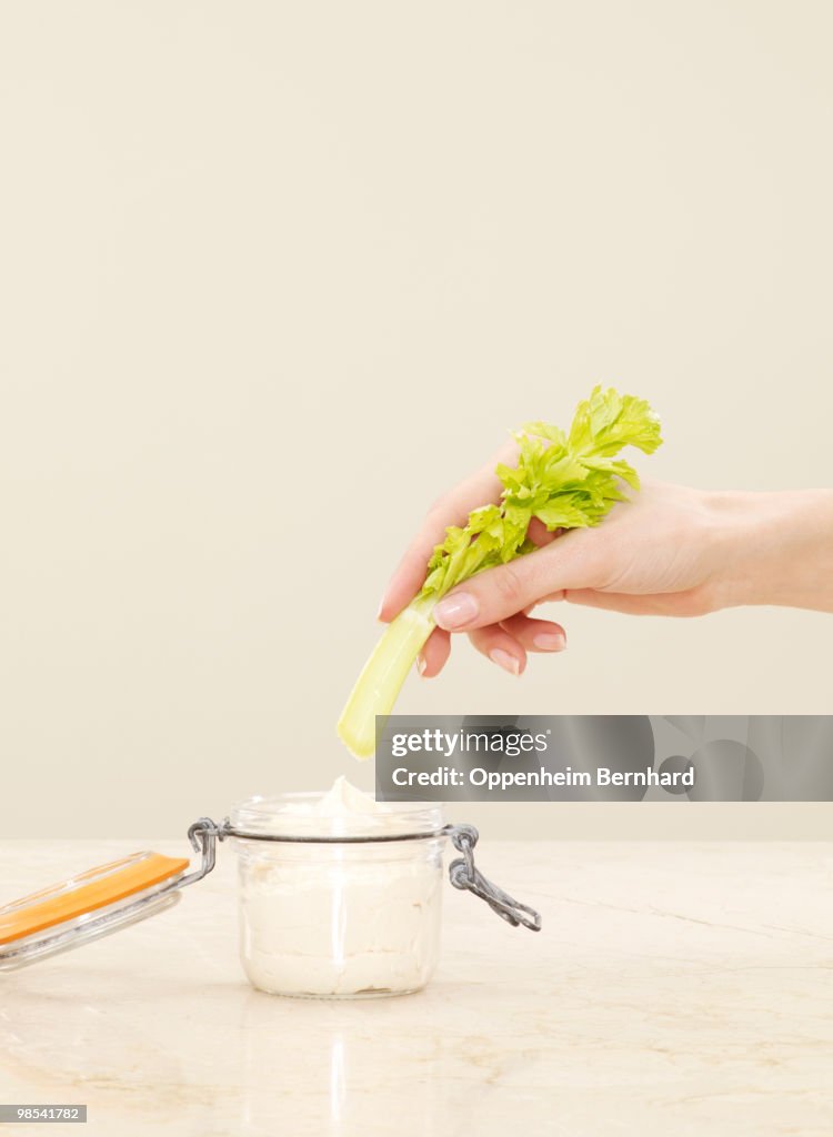 Female hand dipping celery into pot of humous