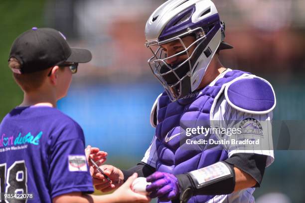 Tony Wolters of the Colorado Rockies signs an autograph for a young fan before a game against the Miami Marlins at Coors Field on June 23, 2018 in...