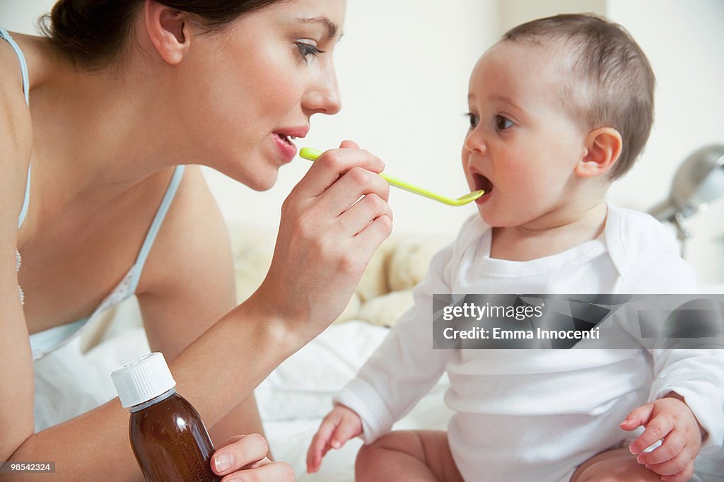 Mum administering syrup to baby in bedroom