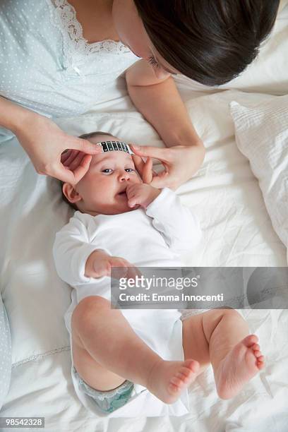mum taking forehead temperature of baby lying down - barefoot feet up lying down girl stock-fotos und bilder