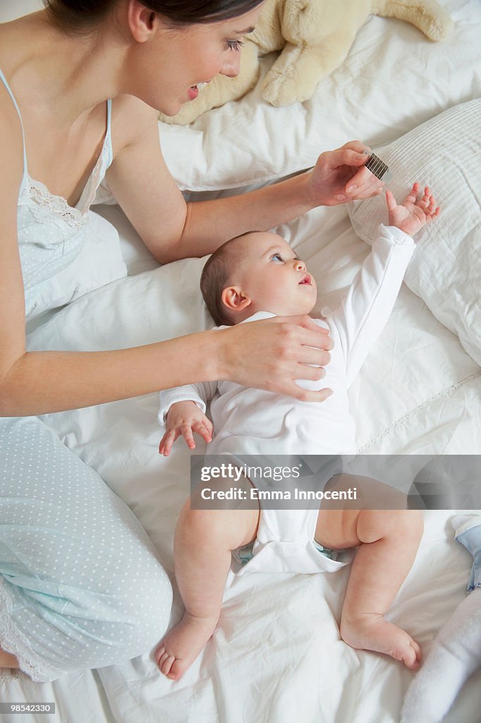 Mum taking temperature of baby lying on bed