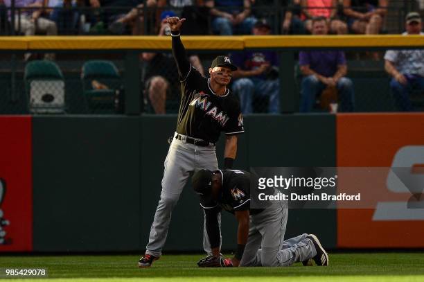 Derek Dietrich of the Miami Marlins signals that teammate Lewis Brinson is OK after a diving catch against the Colorado Rockies at Coors Field on...
