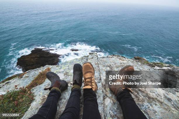 two pairs of feet by a cliff overlooking the sea - pov walking stock pictures, royalty-free photos & images