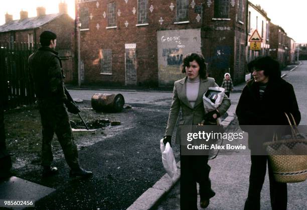 Woman out shopping walk past a British soldier who patrols a derelict street in the sectarian divide of north Belfast, 21st January 1972. Protestant...