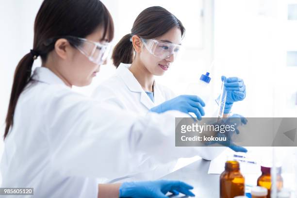 a woman wearing protective equipment which is experimenting with liquid. - measuring cylinder stock pictures, royalty-free photos & images