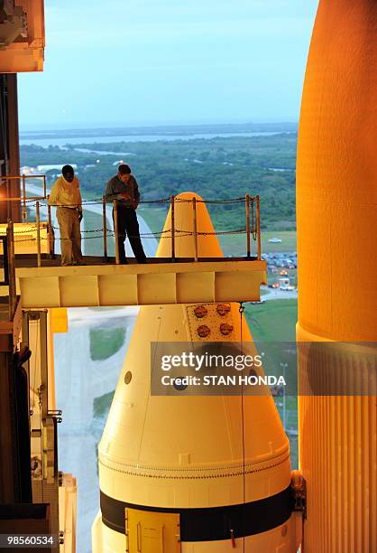 Two men stand near one of the solid rocket boosters and the external fuel tank while the space shuttle Atlantis stands ready in the Vehicle Assembly...