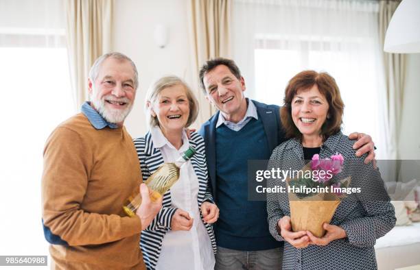 two senior couples holding a bottle of wine and a plant in a pot at home. - pot plant stock pictures, royalty-free photos & images