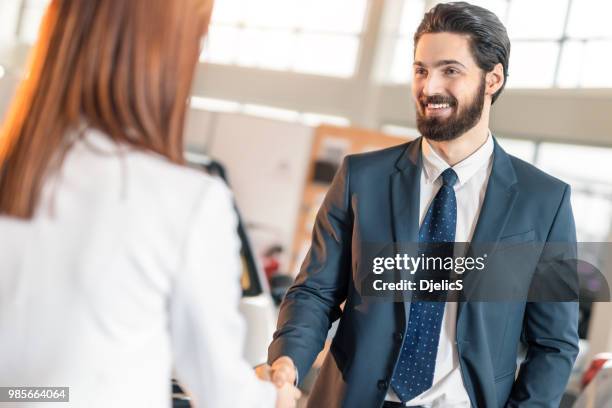 young businessman and businesswoman shaking hands in car dealership. - trade show stock pictures, royalty-free photos & images