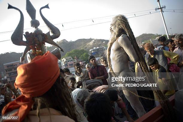 Hindu holy man stands on a bench as Hindu devotees pay their respects to him on the banks of river Ganges during the Kumbh Mela festival in Haridwar...