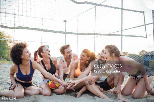 jugadores de voleibol alegre sentado en la playa y poniendo las manos en la pila de - campeón de torneo fotografías e imágenes de stock