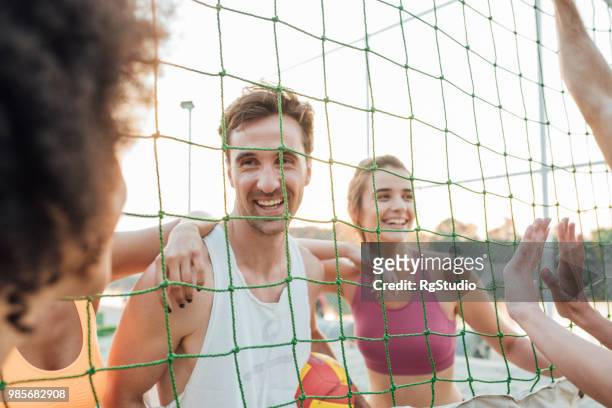 hombre feliz mirando a sus compañeros de equipo a través de la red del voleibol - campeón de torneo fotografías e imágenes de stock
