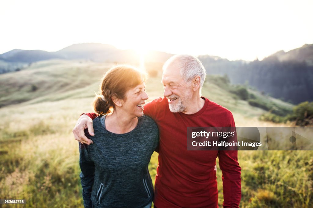 Senior active couple standing outdoors in nature in the foggy morning.