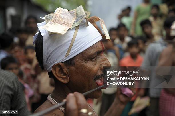 An Indian Hindu devotee adjusts a metal rod pierced through his tongue during the ritual of Shiva Gajan at a village in Bainan, some 80 kms south of...