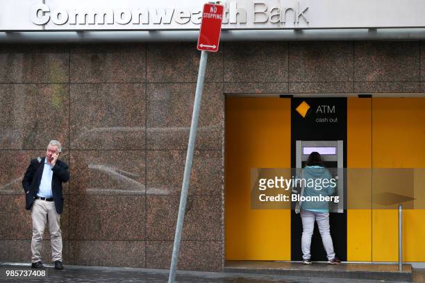Pedestrian uses a phone as a customer uses an automated teller machine at a Commonwealth Bank of Australia branch in the central business district of...