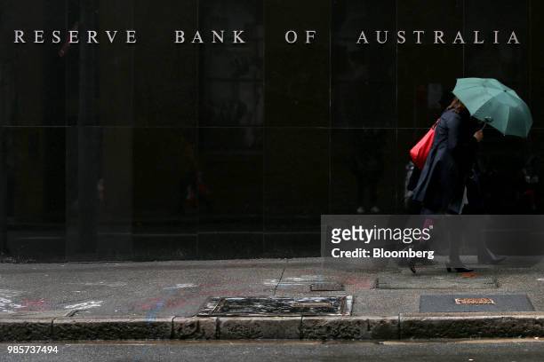 Pedestrians with an umbrella walk past the Reserve Bank of Australia headquarters in the central business district of Sydney, Australia, on Thursday,...