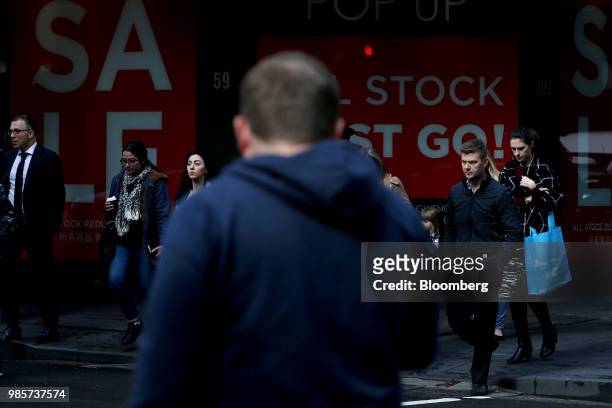 Pedestrians cross a road as sale signs are displayed in a store window on Pitt Street in the central business district of Sydney, Australia, on...