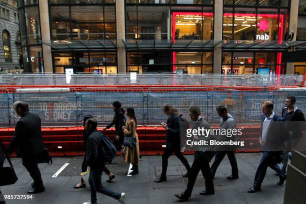 Pedestrians walk past a construction fence near a HSBC Holdings Plc bank branch and a National Australia Bank Ltd. Branch on George Street in the...