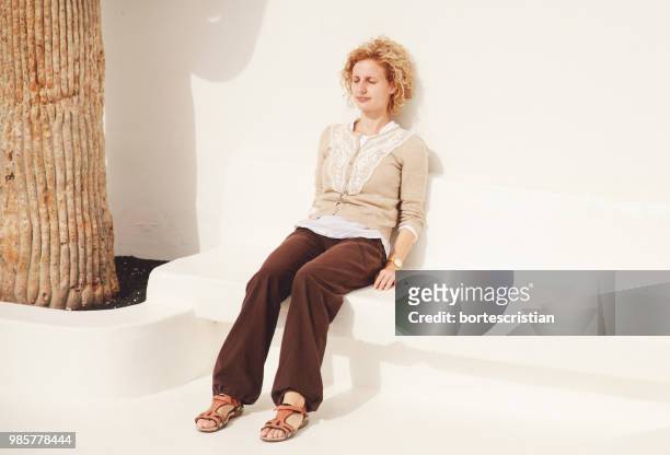 young woman sitting against white wall - bortes fotografías e imágenes de stock