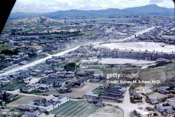 Aerial view of homes, small fields, a large factory, and train lines, Seoul, South Korea, July 1952.