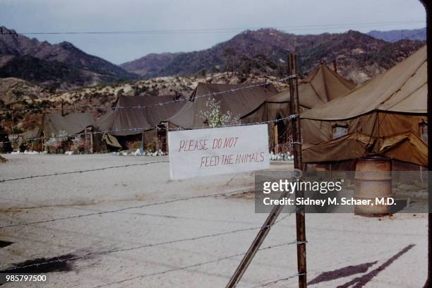 View of a sign that reads 'Please Do Not Feed the Animals' on a barbed wire fence around the officers' compound at the 8063rd MASH , South Korea,...