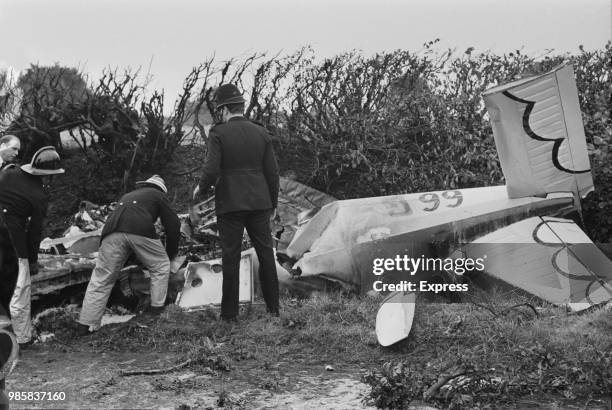 Policemen and firefighters examining the wreckage of Prince William of Gloucester's Piper Cherokee light aircraft after it crashed during competition...