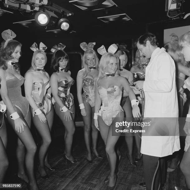 Playboy Bunny waitresses line up to receive a flu vaccine from a medic dressed in a white coat at the Playboy Club in London on 10th October 1972.