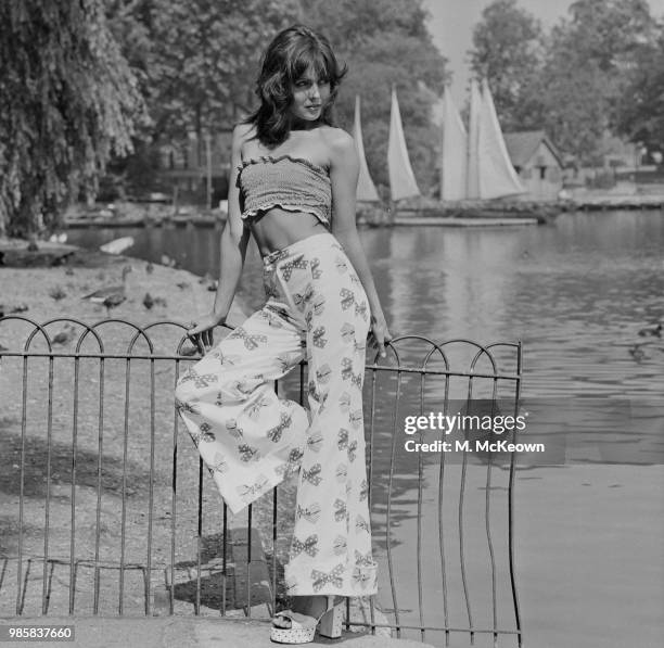 Young female model wears a shirred bandeau boob tube style cropped top with bow motif printed bell bottom high waisted flared trousers and platform...