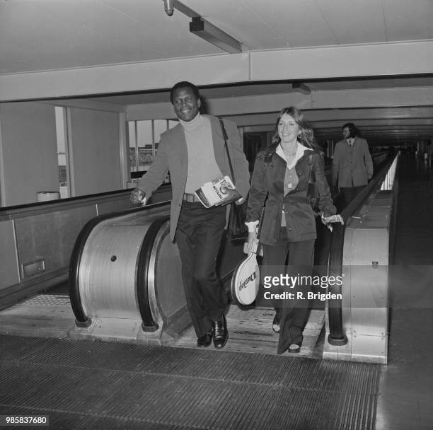 American actor Sidney Poitier and Canadian actress Joanna Shimkus pictured on a moving walkway at Heathrow airport in London on 11th September 1972.