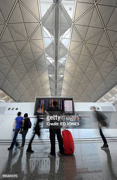 Travellers walk past a flight information board at Hong Kong's international airport on April 21, 2010. Thousands of frustrated passengers crowded...