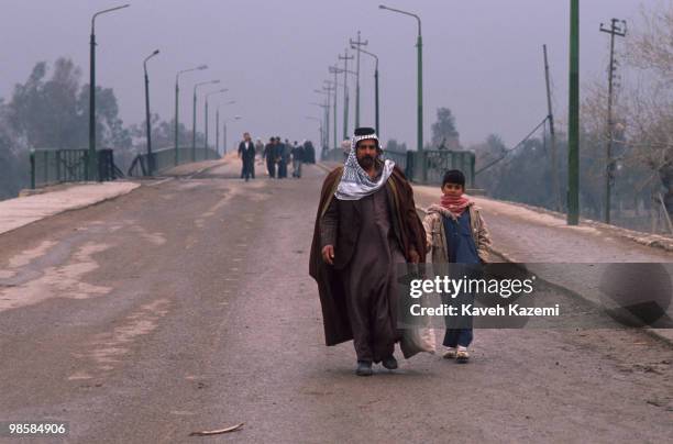 An Iraqi man in traditional costume walks with his son on a bridge partly damaged by Allied bombing raids, in central Baghdad during the Gulf War,...