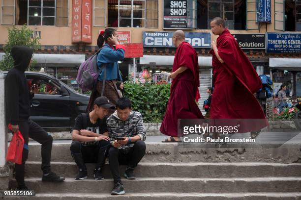 Bhutanese teens are seen hanging out using mobile phones as monks stroll by on June 14 in Thimphu, Bhutan. While many are expected to wear the "Gho"...