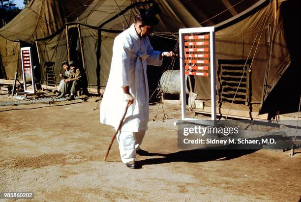 View of American military surgeon Captain Sidney Schaer , of the 8063rd MASH , dressed in traditional Korean clothing as he smokes a long pipe...