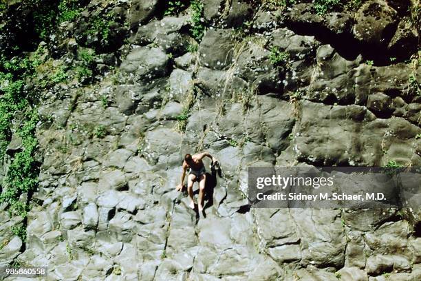 View of Dick Koons, of the 8063rd MASH , in a swimsuit, as he climbs down a rock wall, South Korea, January 1952.