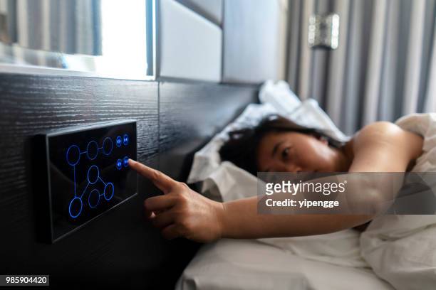woman sleeping on bed, pushing button to open curtain