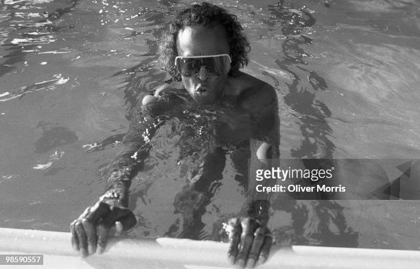 American jazz musician Miles Davis swims, still in his sunglasses, in the health club atop the UN Plaza Hotel, New York, New York, mid 1980s.